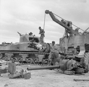 A 75mm gun being salvaged from a knocked-out Sherman tank at 26th Armoured Brigade workshops in Perugia, 30 June 1944. The entry point for an 88mm shell can be seen on the side of the tank's hull. © IWM (NA 16518)